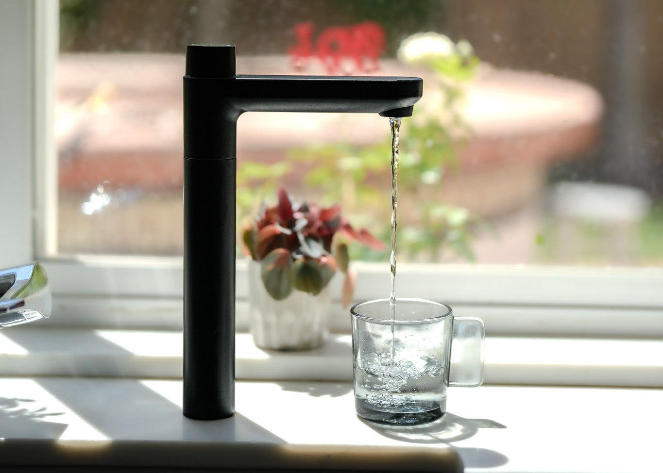 Black faucet pouring water into a glass on a kitchen counter with a blurred background